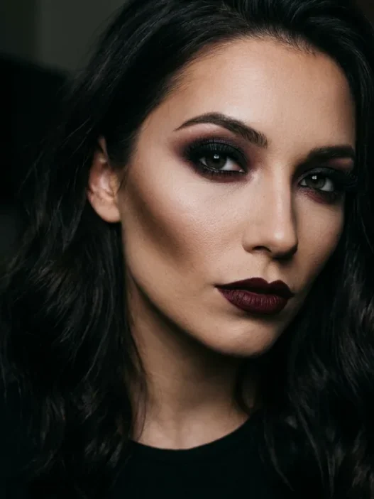 Woman with complete dark feminine makeup featuring smoky charcoal eyes and wine-toned lips