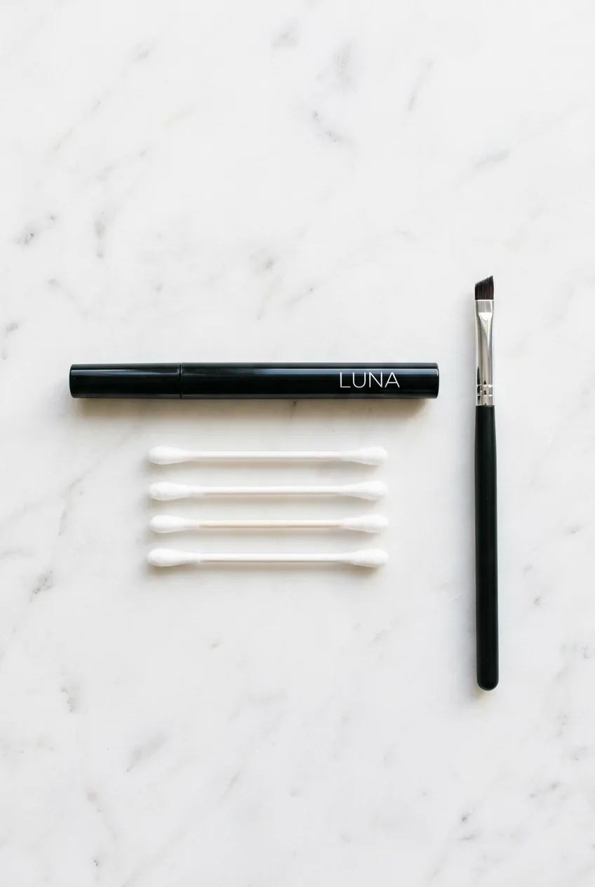 Essential eyeliner tools arranged on marble surface including liquid pen, cotton swabs, and brush