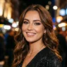 Woman with finished evening glam makeup featuring smoky eyes and nude lips in warm city lighting