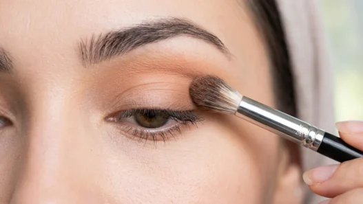 Fluffy makeup brush blending transition shade into eye crease with soft gradient forming