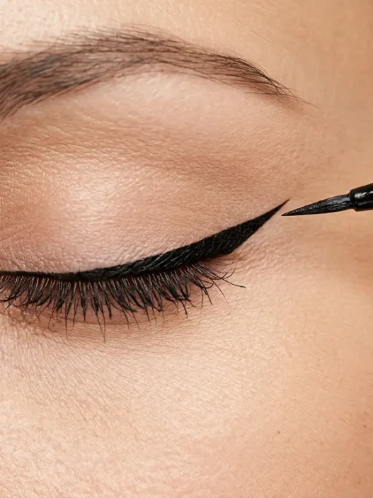 Liquid eyeliner brush creating precise winged tip at outer corner of closed eye with clean line