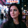 Woman with goth makeup featuring black lipstick and dramatic eyeliner in neon-lit urban setting