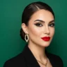Woman with polished red carpet makeup featuring bold lips and defined features against emerald green background