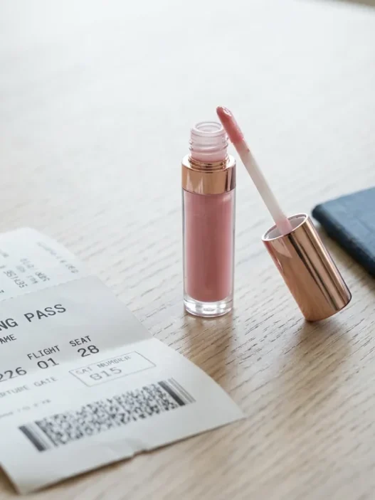 Travel-sized lip gloss tube next to boarding pass and passport on white surface