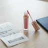 Travel-sized lip gloss tube next to boarding pass and passport on white surface