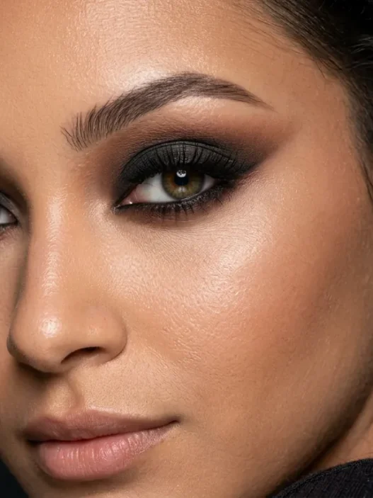 Close-up beauty portrait showing dramatic smoky eye makeup with deep blended shadows in dark moody lighting