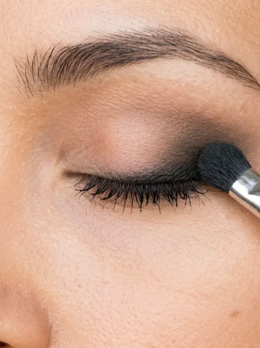 Close-up of smudger brush blending black kohl pencil along woman's lash line creating soft smoky gradient