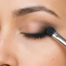 Close-up of smudger brush blending black kohl pencil along woman's lash line creating soft smoky gradient