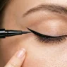 Close-up of liquid eyeliner brush creating precise winged flick at outer corner of closed eye