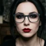 Woman wearing glasses with dramatic vampire makeup showing dark eyeshadow and deep red lips in gothic lighting