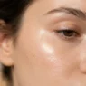 Extreme close-up of luminous dewy skin with sharp cheekbone highlight and glassy healthy glow in warm light