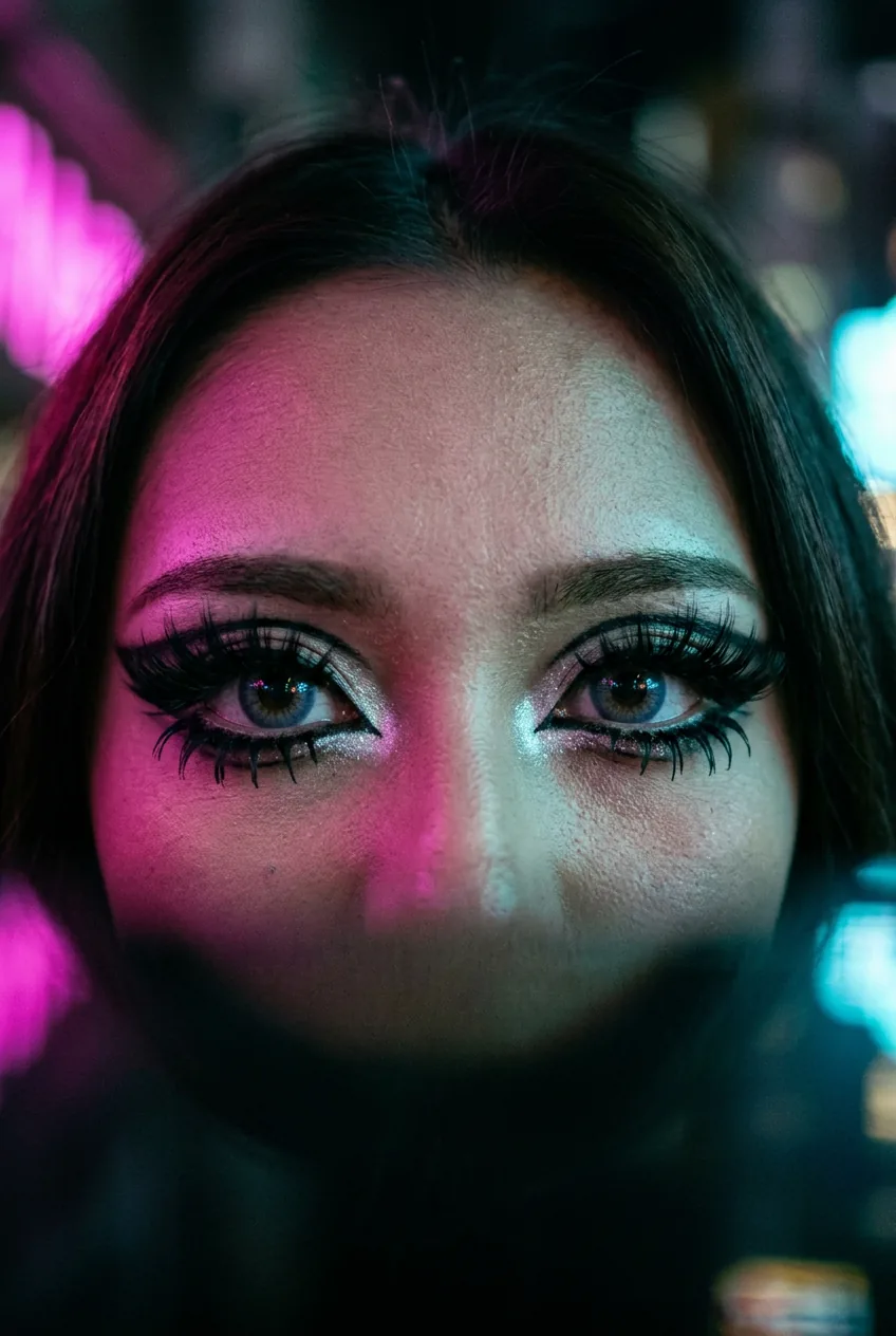 Extreme close-up of dramatic gyaru eye makeup with layered false lashes and pale inner corner highlight in magenta light