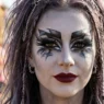 Woman wearing dramatic zombie-inspired makeup with ashen grey skin deep burgundy lip and graphic dark eyes in editorial close-up