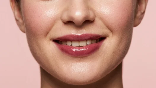 Woman with sheer berry balm on smiling lips in soft beauty light