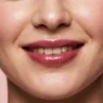Woman with sheer berry balm on smiling lips in soft beauty light