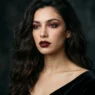 Woman with dark wavy hair wearing oxblood lipstick and berry smoky eyes in moody light