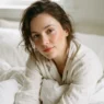 Woman with fresh dewy clean makeup and peach blush resting in white bedding