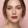 Woman with fresh natural glam makeup featuring dewy skin and glossy berry lips on pink background