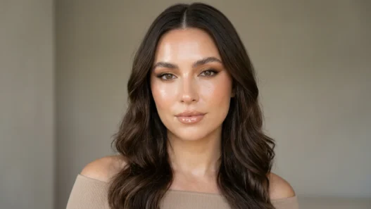 Woman with glassy dewy skin and mirror-shine nude lips in soft daylight