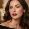 Woman with soft holiday glam makeup featuring satin skin and glossy berry lips in warm light