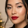 Woman with classic red lips and champagne eyeshadow glowing in warm holiday light